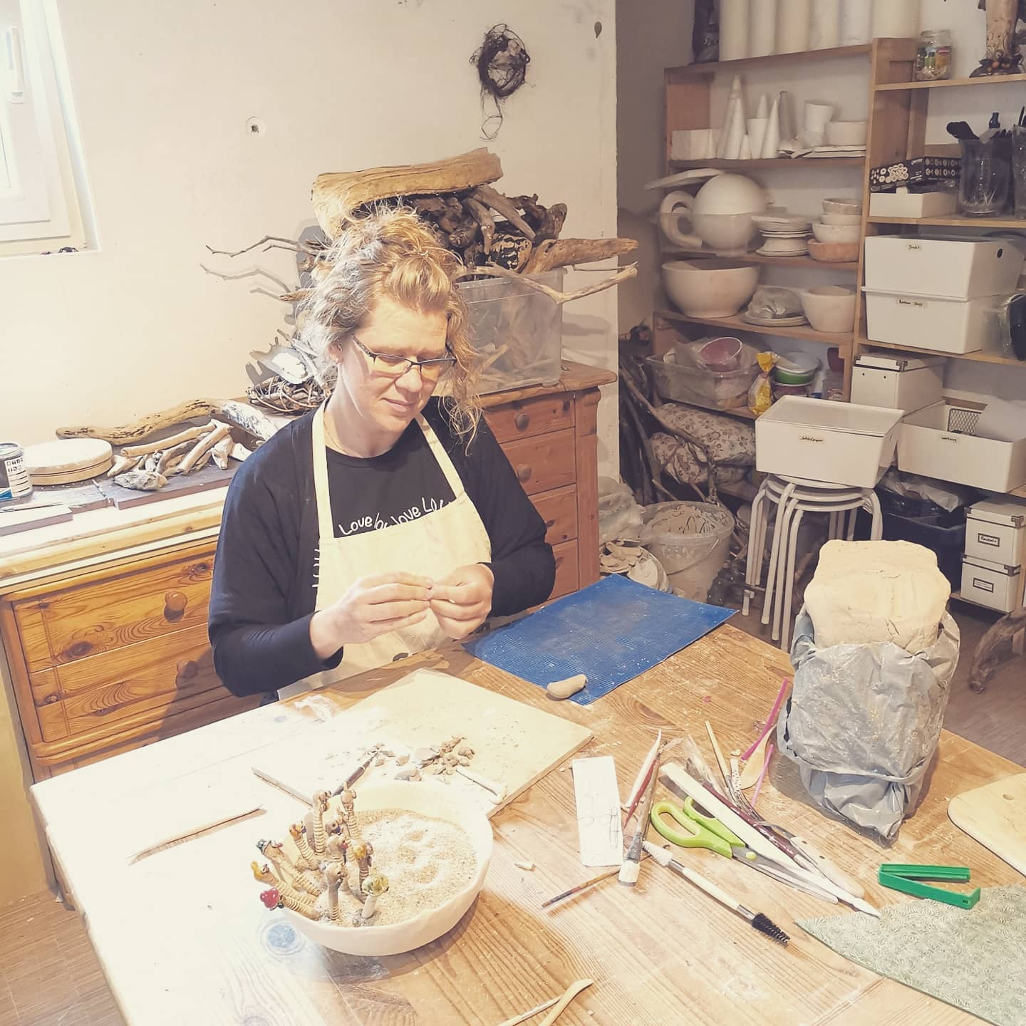 Martina Heinl bei der Arbeit. Am Tisch in ihrer Werkstatt sitzend arbeitet die Keramikkünstlerin an ihren schräger Vögeln, Mohnblütenkeramik, fleischfressende Pflanze oder Wattwürmer, wie sie sich keck aus dem Sand emporheben - als Gartenstecker zum Beispiel.