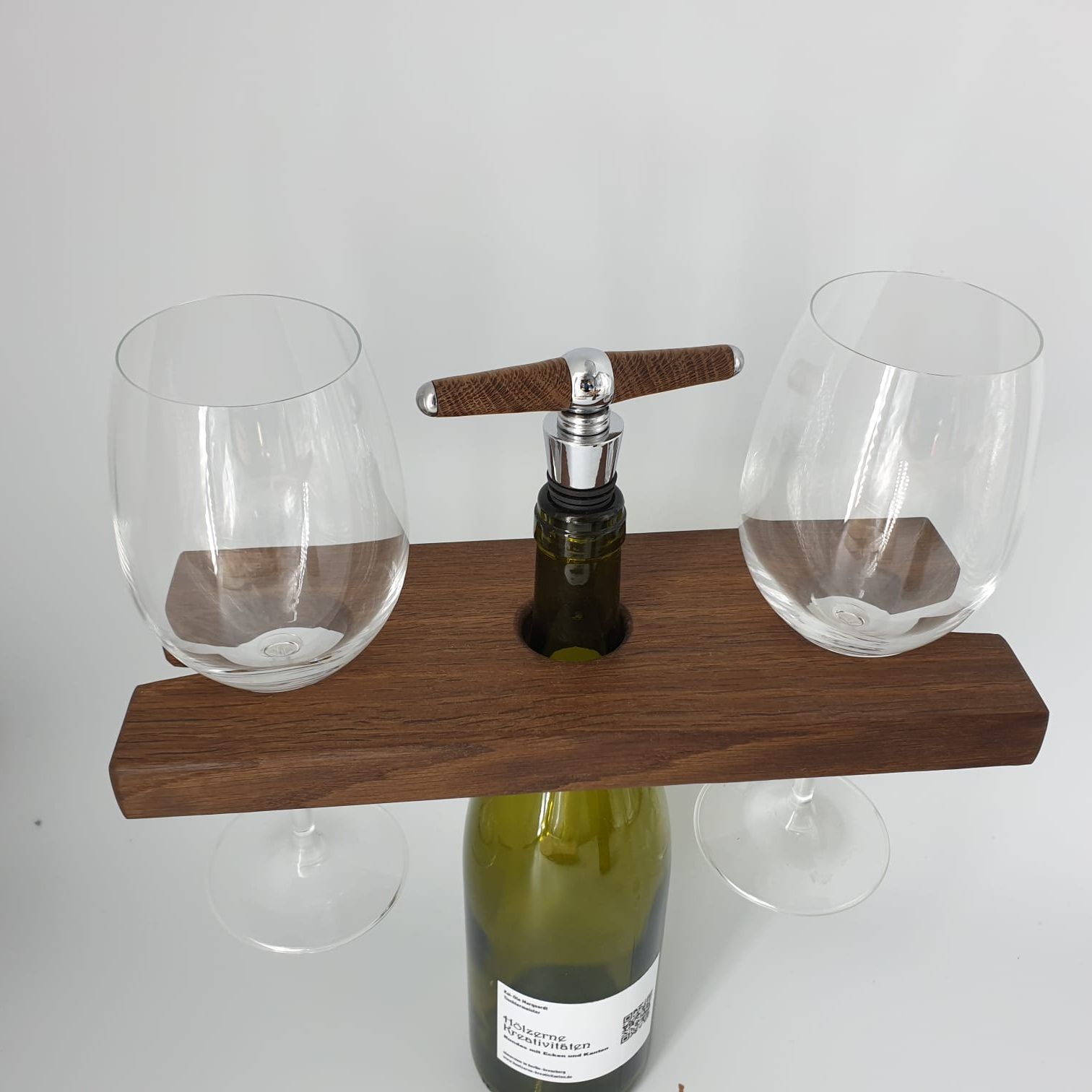 Kai-Ole Marquardt Glashalter besteht aus einer Flasche Wein, der ein Brett übergestülpt ist, in das links und rechts je ein Weinglas eingehängt ist. Die Weinflasche hält den Korkenzieher. Ein großartiges, weil platzsparendes Modell für ein Picknick im Grünen. Kai-Ole Marquardt betreibt