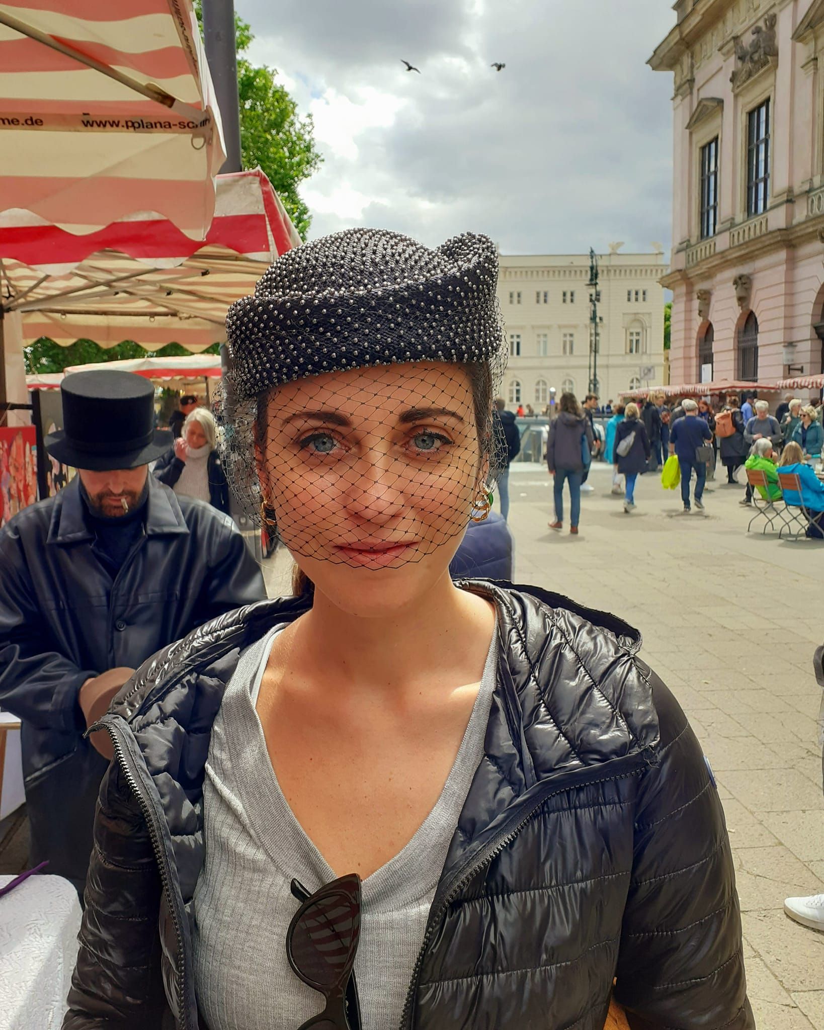 Carlos Klein: Junge Frau, die etwas auf sich hält. Tropfenförmige Hutkrempe mit Netz vor dem Gesicht - alles in Schwarz gehalten.