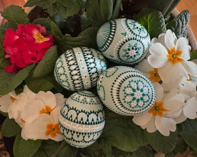 Sorbische Ostereier in Türkis und Weiß liegen zwischen grünen Blättern und bunten Frühlingsblumen