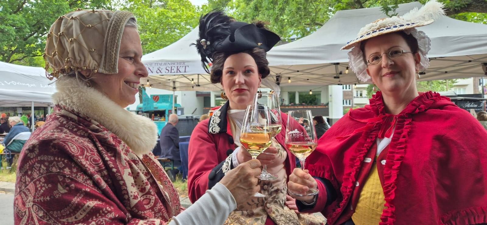 Die Damen der Höfischen Gesellschaft erheben sich stilvoll und lassen ihre Weingläser beim WeinPfingsten 2025 fröhlich erklingen