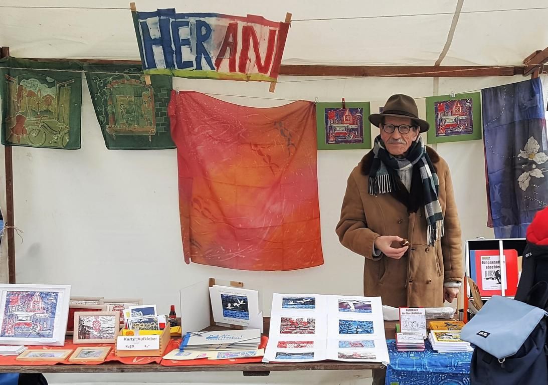 Herbert Friedrich Witzel ist Verlagsinhaber von Worttransport.de. Dieses Bild ist auf dem Kunstmarkt am Karl-August-Platz aufgenommen. Herbert Witzel steht bei den Batikarbeiten seiner Frau und stellt den Besuchern seinen Vorlag vor. Die Linoldrucke von Antje Witzel zieren die Buchcover und die Seiten seiner Bücher.