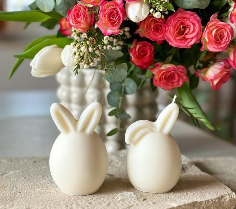 Alina Döhnel macht formschöne Kerzen aus Sojawachs.  Zu sehen zwei weiße Hasen in Kugelform vor roten Blütenpracht.