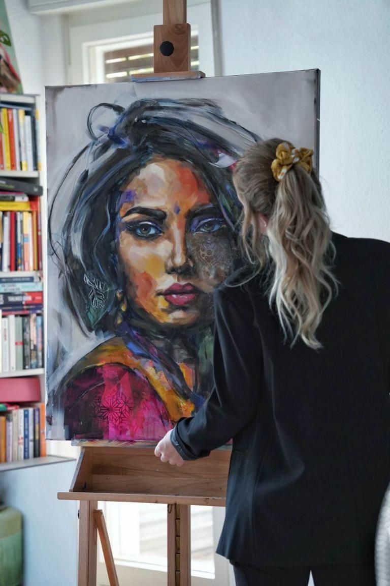 Jana Voscort malt an einem Bild, das eine junge, schöne Frau darstellt. 