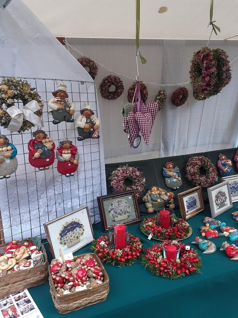 Wir beleuchten einen Teil von Ursula Reddmanns Kunststand: Es sind Kränze aus Hagebutten und dicker, roter Kerze in der Mitte, Trockenblumenkränze an der Rückwand des Marktstands.