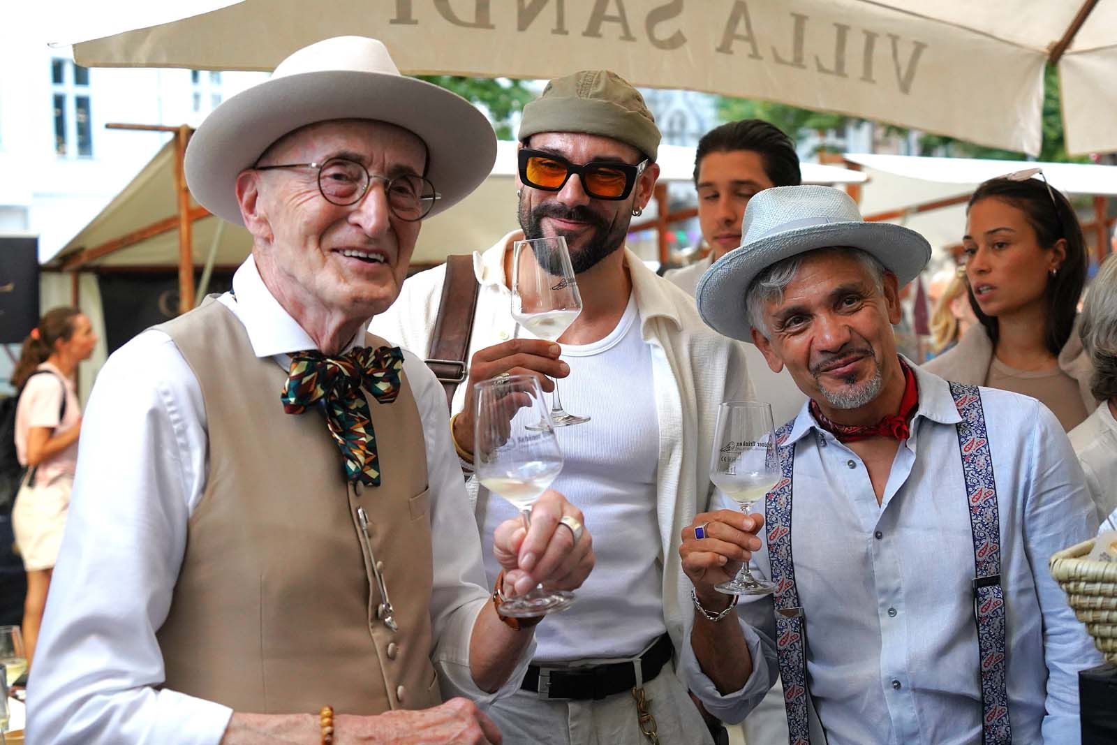Günther Krabbenhöft hat die Einladung zum Sommerfest in der Leonhardtstraße gern angenommen. Stilgerecht mit weißem Hemd, beige-brauner Weste, Fliege und hellem Hut lässt er sich fröhlich auf eine Weinprobe ein.