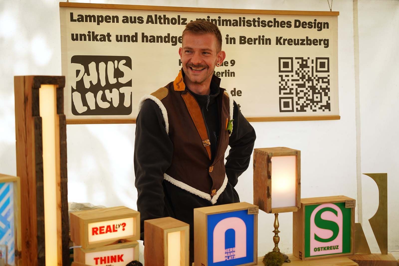 Phil hinter seinem Marktstand mit handgefertigten Lampen aus Altholz und leuchtenden Schriftzügen