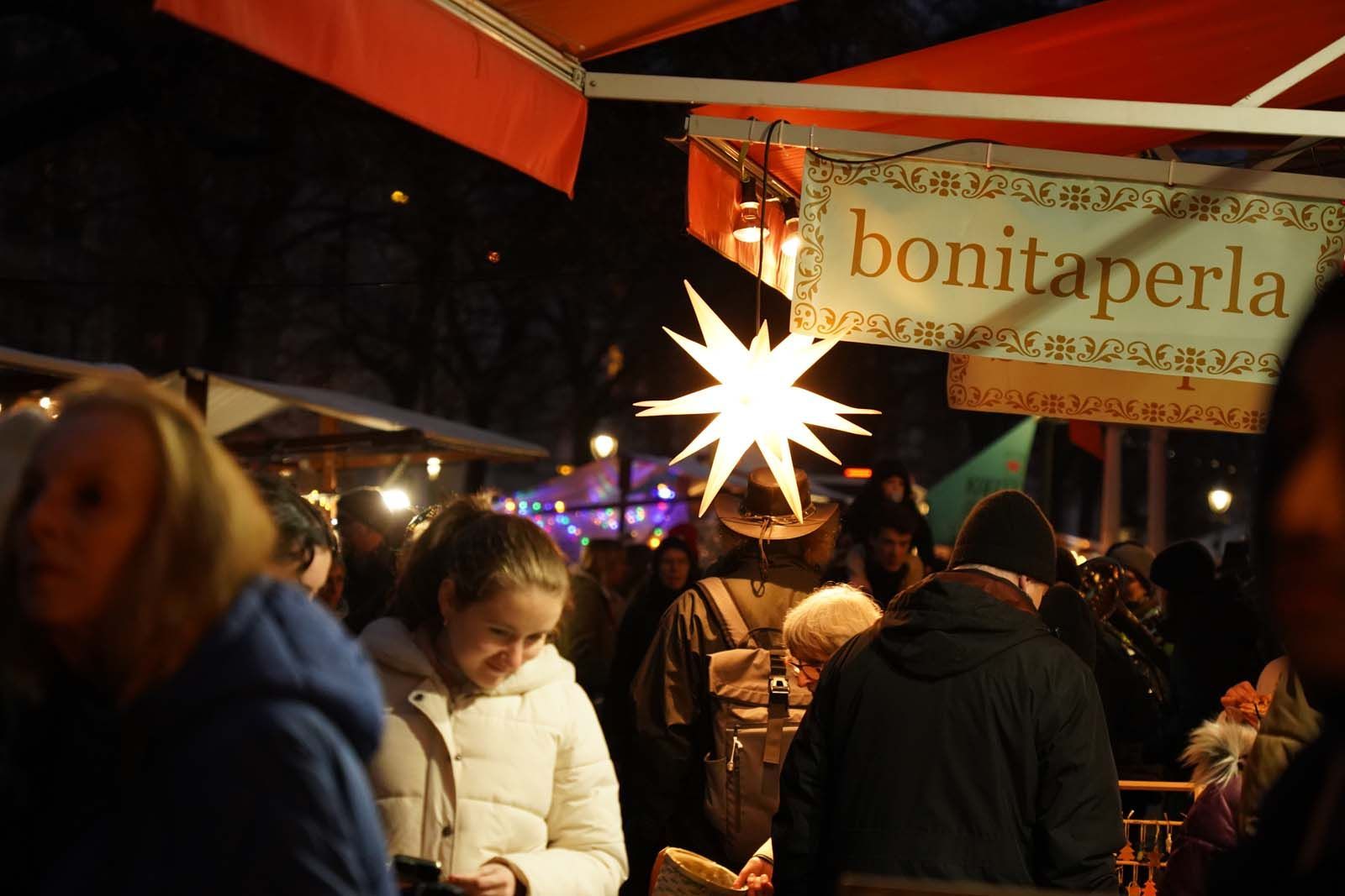 ADVENT-Markt mit Lichterglanz: Besucher:innen vor dem festlich beleuchteten bonitaperla-Stand in der Leonhardtstraße