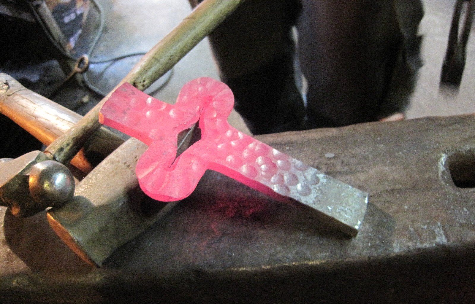 Ein schmiedeeisernes Kreuz, noch rotglühend aus der Gluthitze, liegt auf dem Amboss – bereit für den nächsten Hammerschlag auf dem Weg zur endgültigen Form