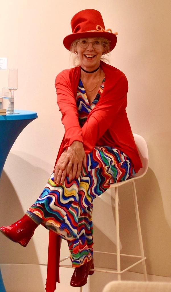 Sylke Bach lacht - ein schöner Anlass, sie mit der Kamera festzuhalten Sylke Bach, offen lachend, roter Stoffzylinder mit gewolltem Knick, roter Jacke und bunter weilläufiger Hose, die Schuhe sind rote Lackstiefel.