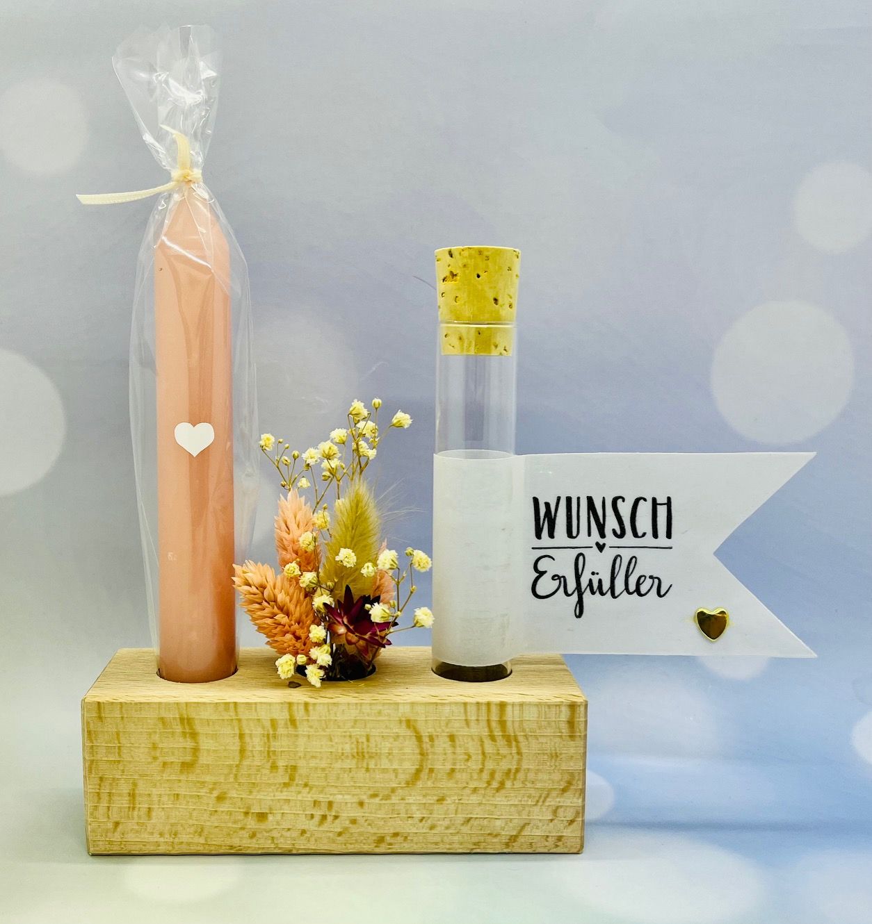 Tanja Specks Wunscherfüller. Eine aprikotfarbene Kerze steht in einem Holzblock versenkt. Ein Wimpel ziert die Aufschrift Wunscherfüller. Und dazwischen steht ein kleiner niedlicher Trockenblumenstrauß.