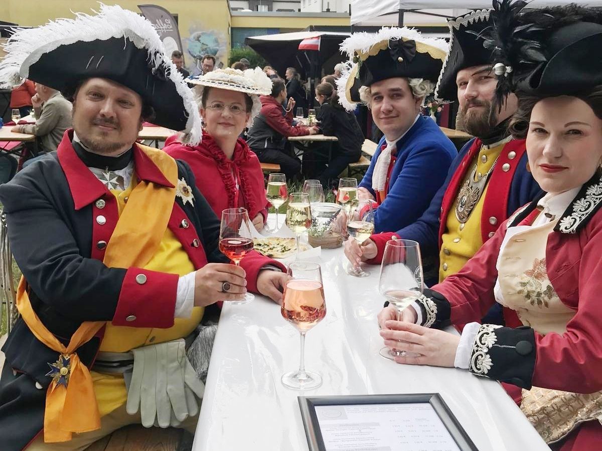 Die Höfische Gesellschaft sitzt beisammen und genießt Roséwein vom Weingut Sommer beim WeinPfingsten in Westend
