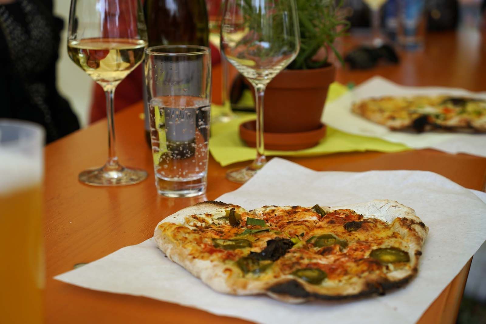 Die Höfische Gesellschaft läutet genussvoll die zweite Runde ein: Weißwein im Glas, Pizza von Duennes Brot auf dem Tisch