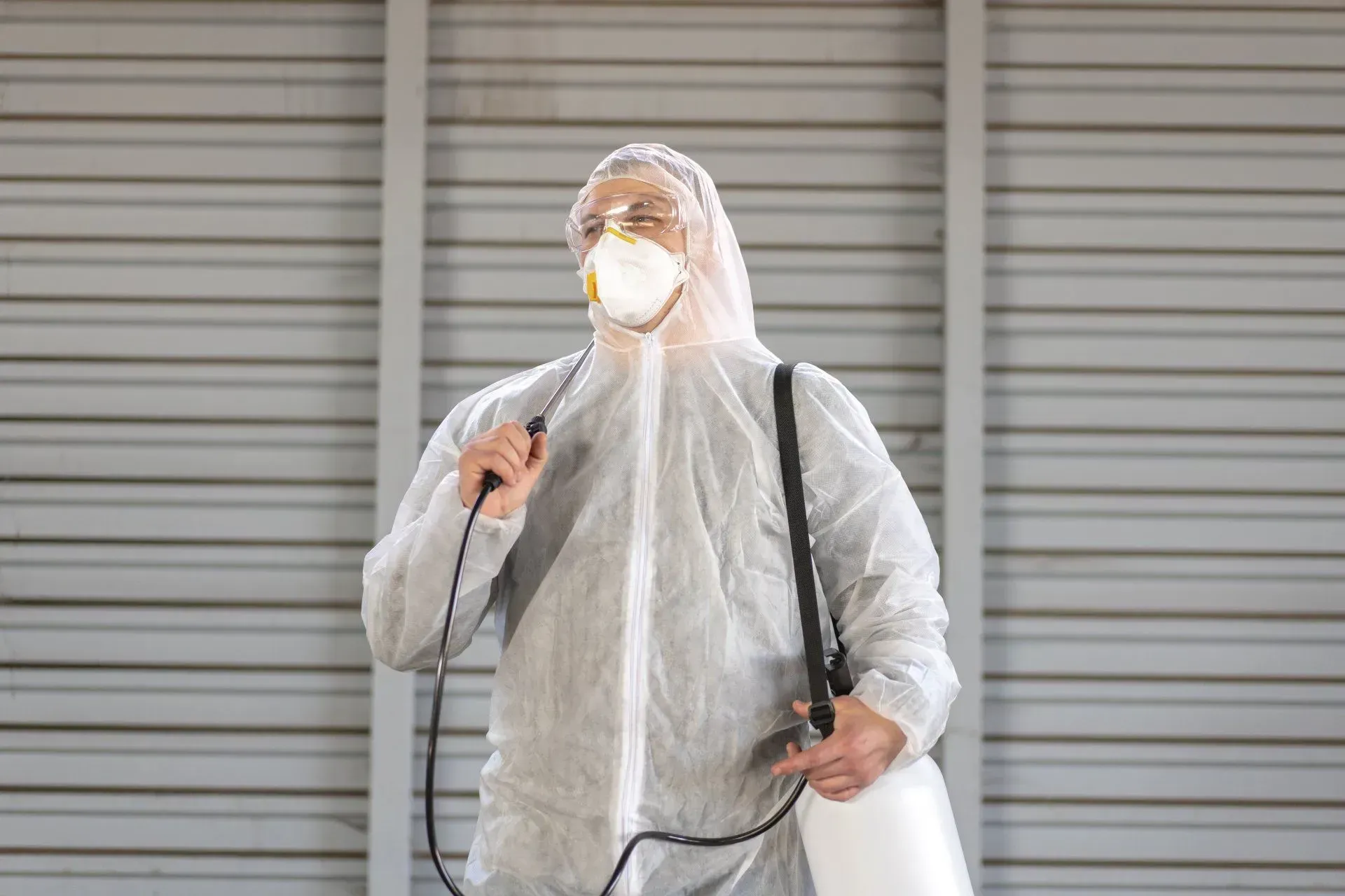 Homme-avec-une-combinaison-et-un-masque-blanche-et-un-pulvérisateur-sur-le-dos