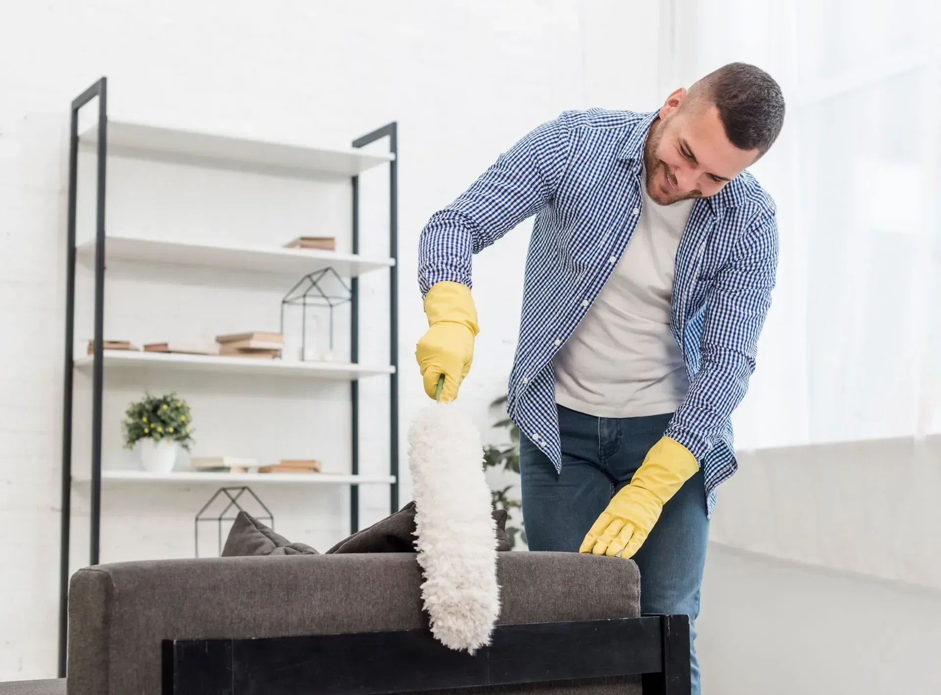 Homme-qui-dépoussière-un-canapé-avec-un-plumeau-blanc-et-des-gants-jaune