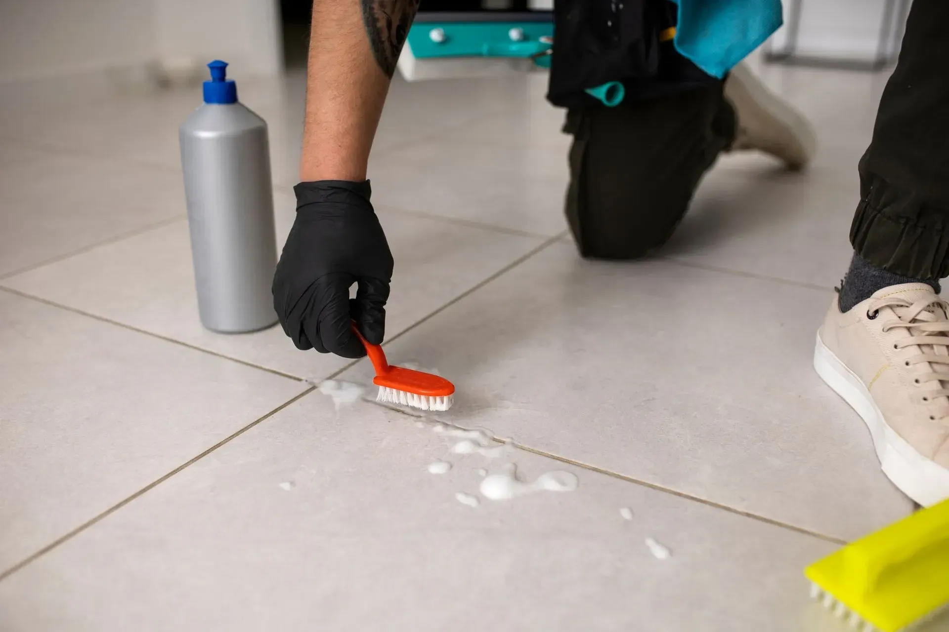 Main-avec-gant-noir-et-une-brosse-qui-nettoie-avec-un-produit-les-joints-d'un-carrelage