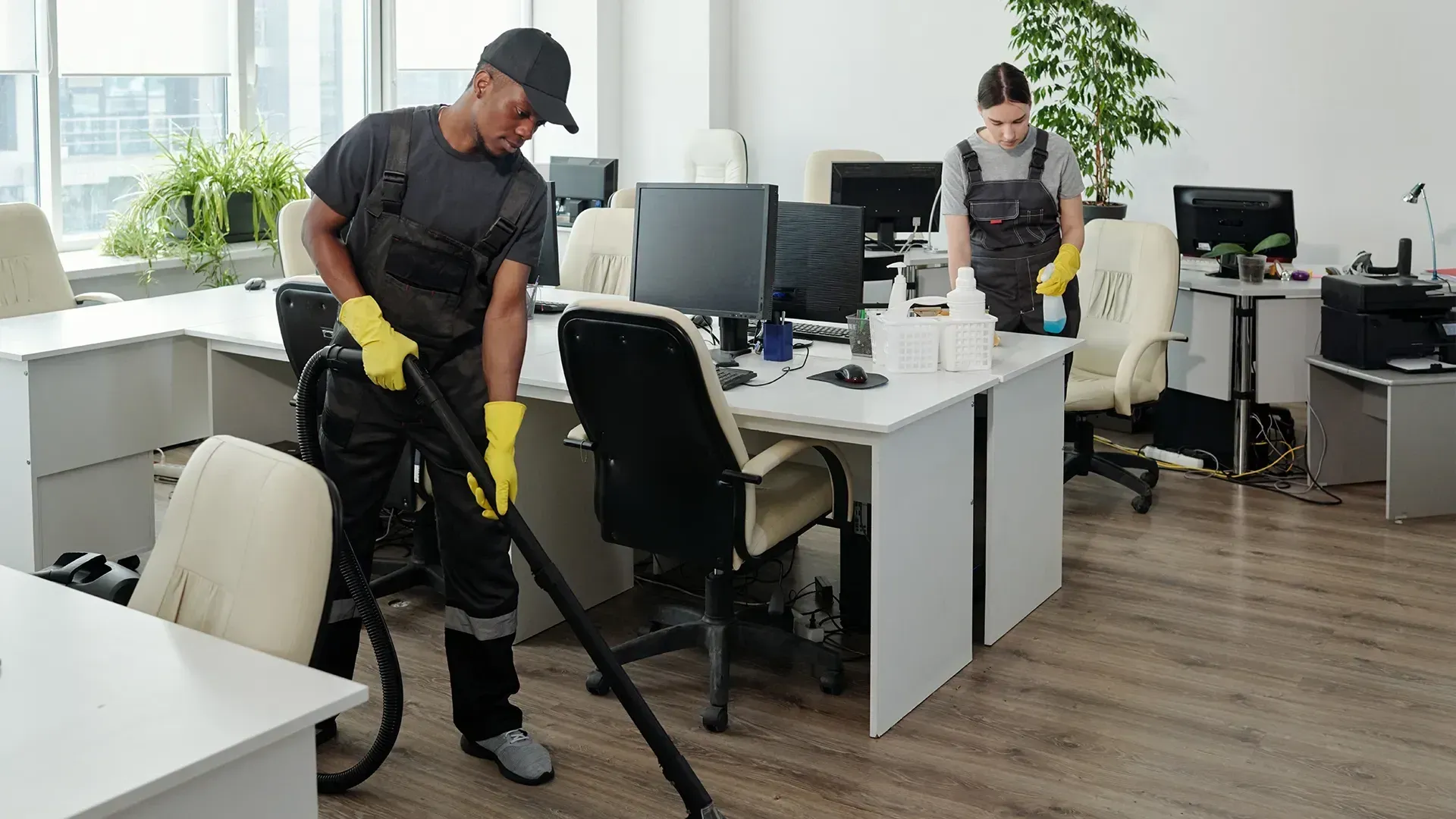 Un-homme-habillé-d'une-salopette-noir-qui-porte-des-gants-jaune-et-qui-passe-l'aspirateur-sur-les-sols-d'un-bureau
