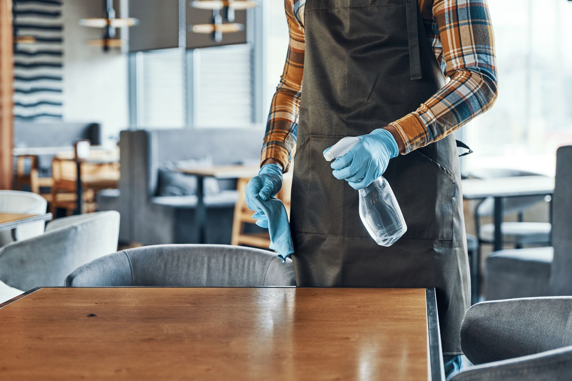 Un homme qui désinfecte les table d'un restaurant avec un chiffon et un produit