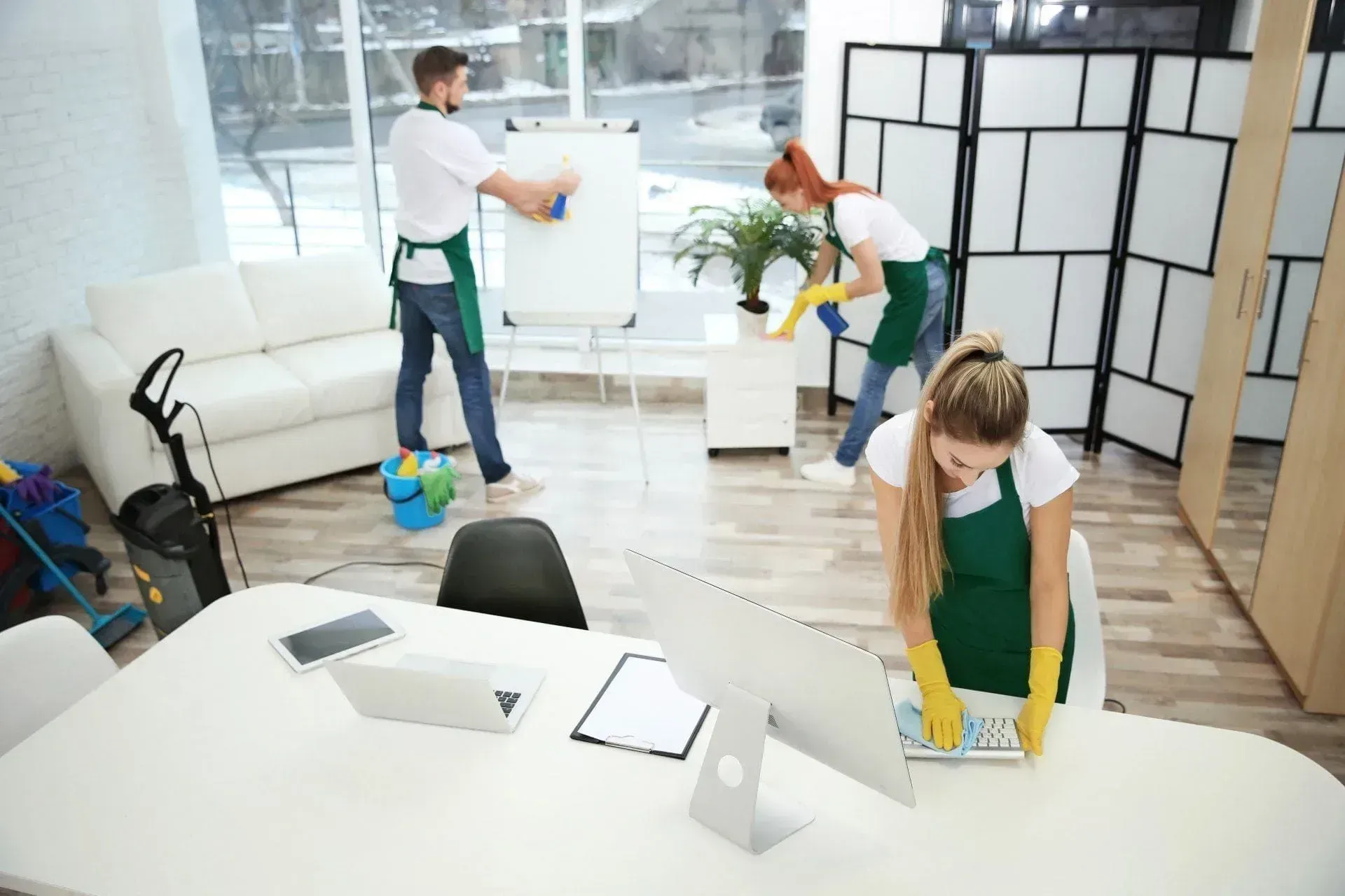 Trois personnes nettoyant un bureau avec des produits de nettoyage