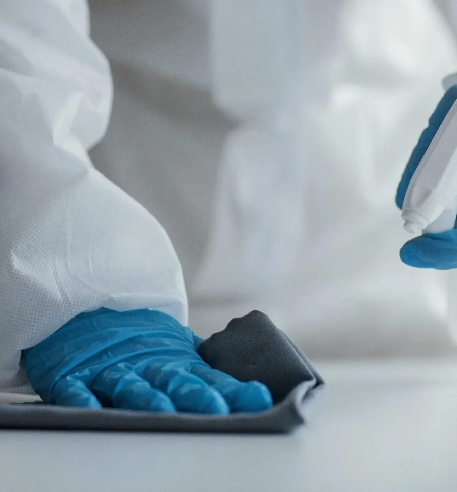 main avec gant bleu utilisant un spray de nettoyage