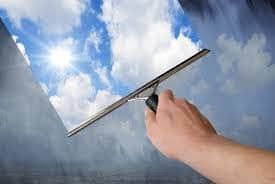 Une main qui passe une raclette pour nettoyer la vitre