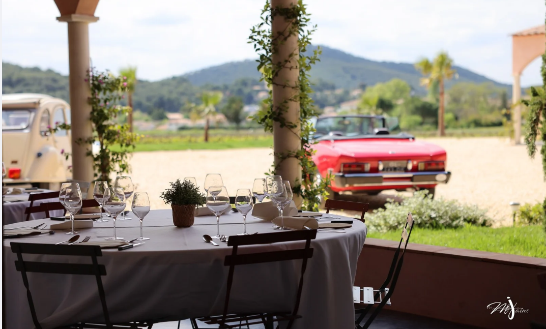 Table dressée en extérieur au Domaine Pieracci, avec vue sur le vignoble et une voiture ancienne rouge en arrière-plan.