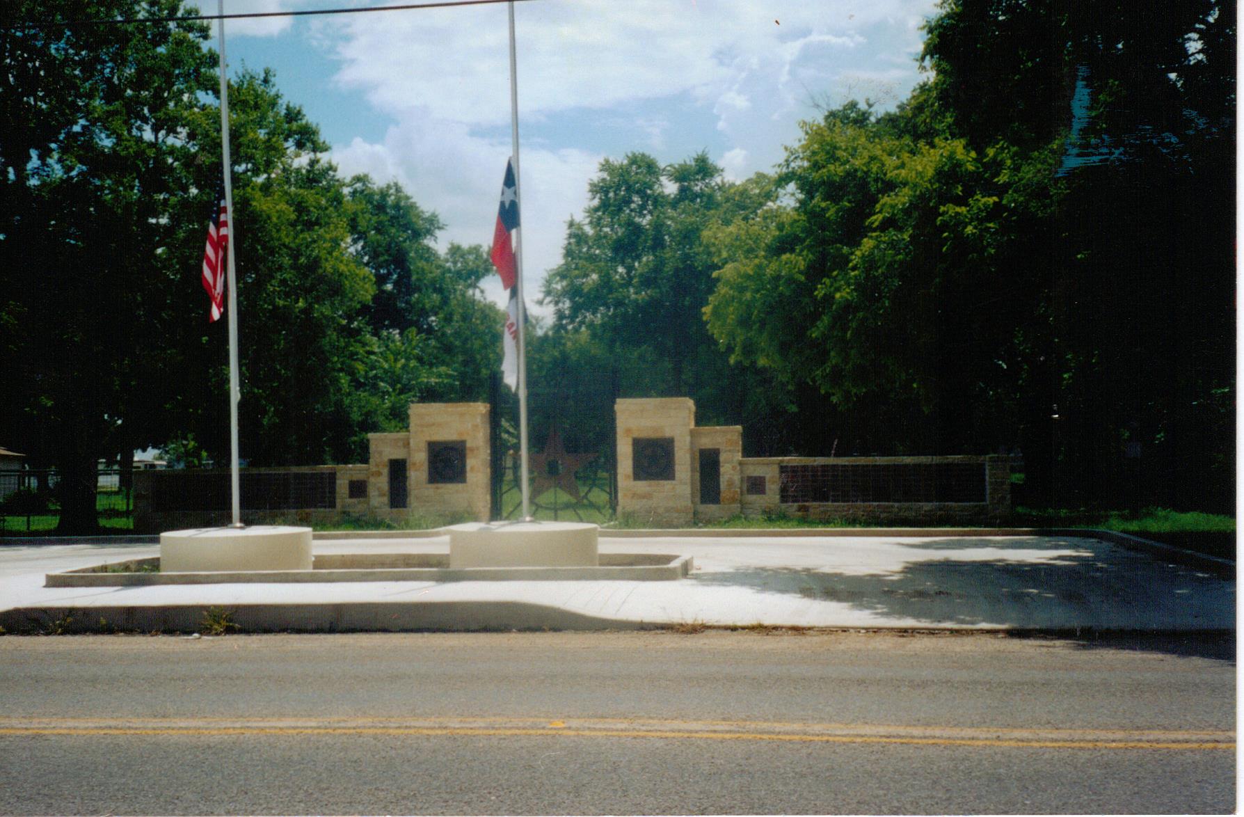 entry gate to Center Point Heritage park, large limstone and iron gate with flagpole in front flying the Texas flag