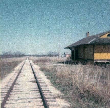 old color picture of the train depot near the tracks with high grass
