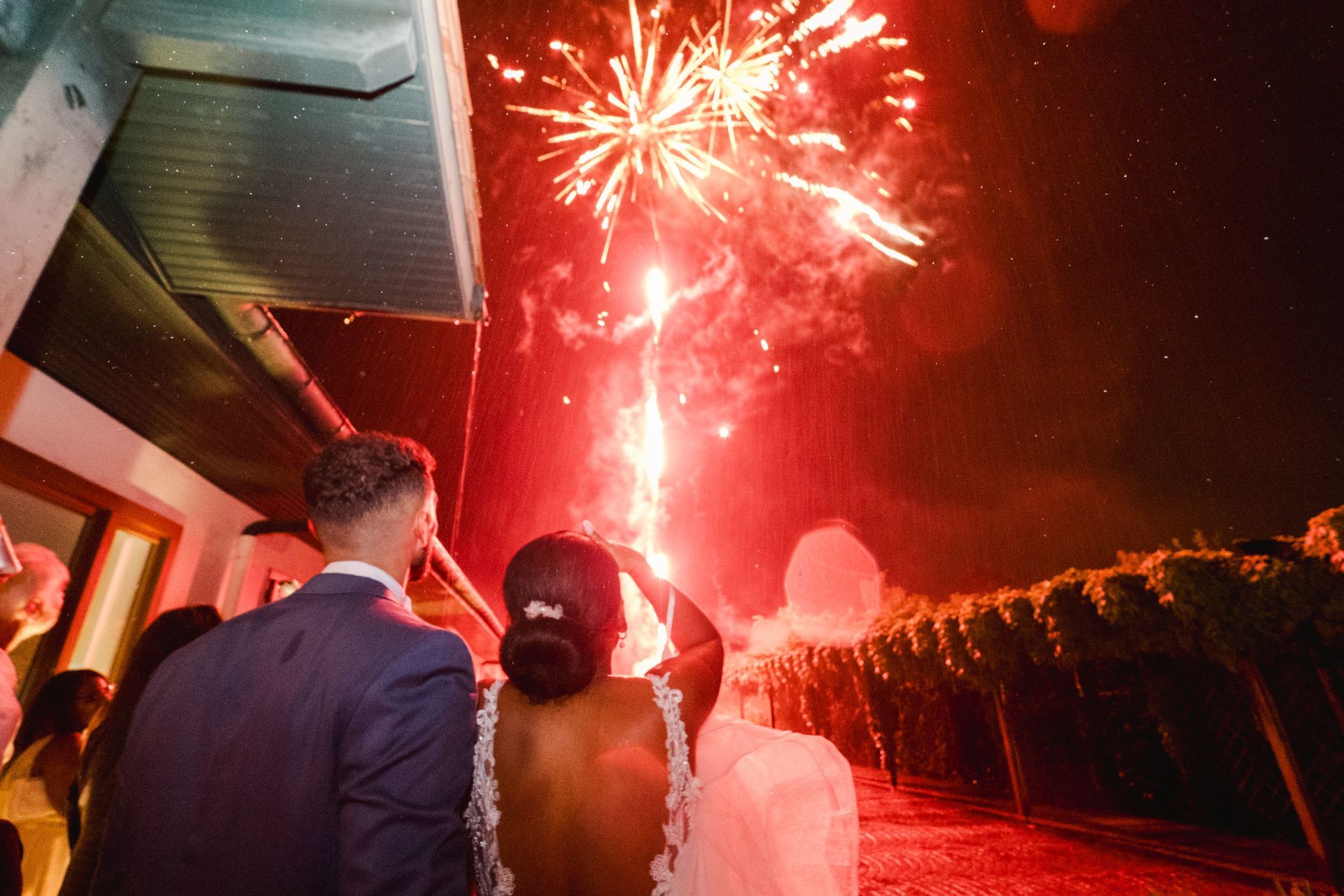 Animation mariage Photo d'un couple de mariés le soir de leur mariage, il fait nuit et les mariés sont dos au photographe, en train de regarder un feu d'artifice rouge