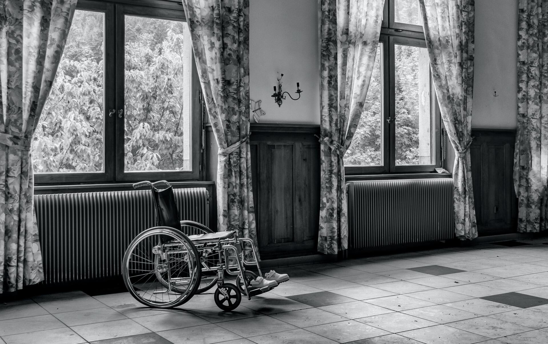 Rollstuhl in leerem Zimmer mit großen Fenstern