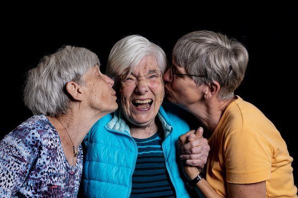 Zwei Frauen küssen eine lachende ältere Frau auf die Wange.