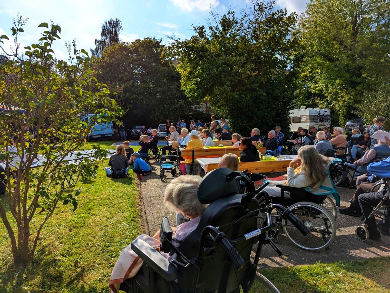 Viele Bewohner und Gäste sitzen im Garten auf Bänken und Stühlen und schauen gemeinsam einer Aufführung zu.