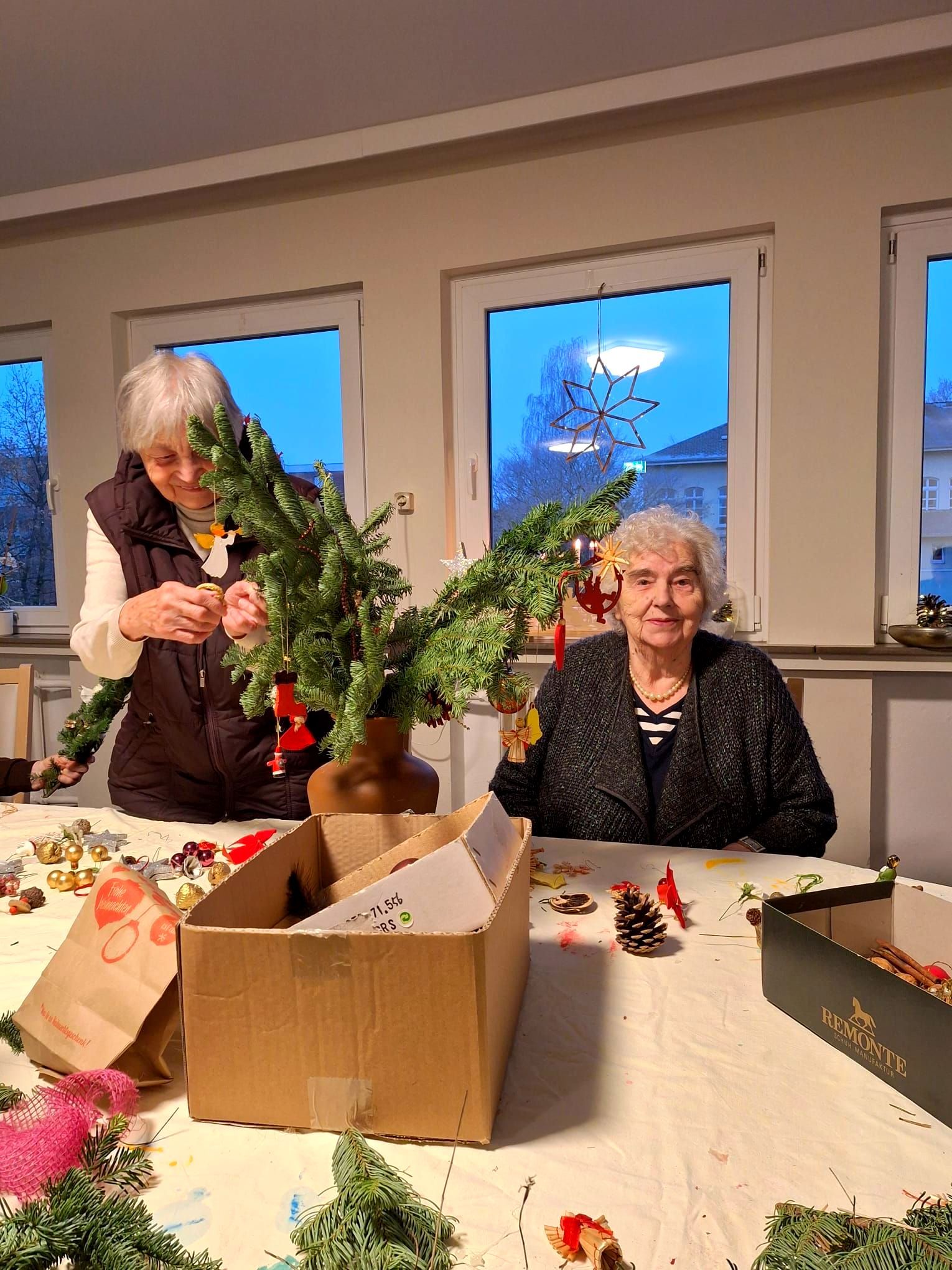 Bewohnerinnen schmücken gemeinsam einen Tannenzweig mit Weihnachtsanhängern.
