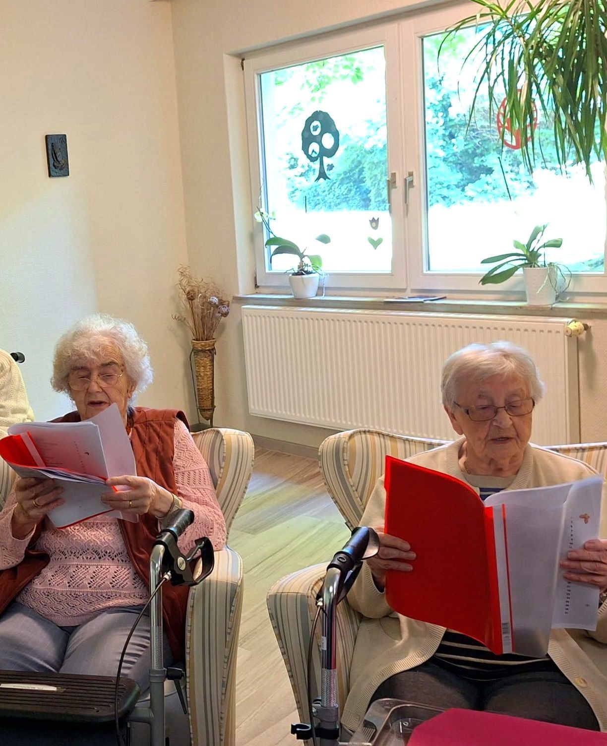 Bewohnerinnen des Lambertistifts sitzen zusammen und singen aus roten Mappe.