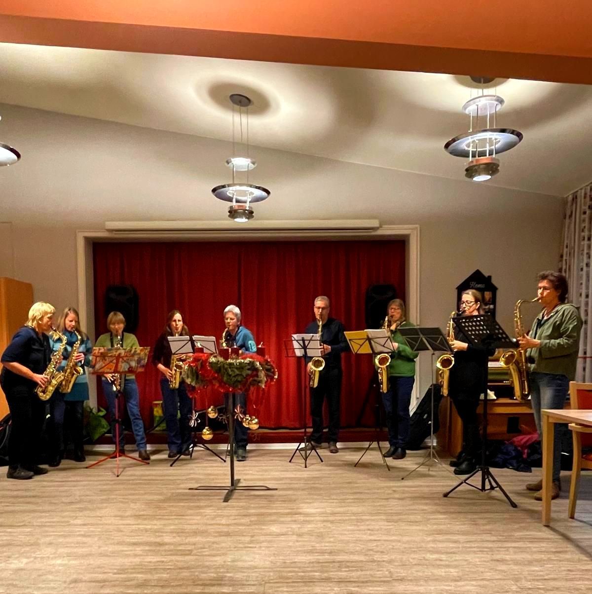 Mehrere Musiker spielen gemeinsam Saxophon vor einem roten Vorhang.