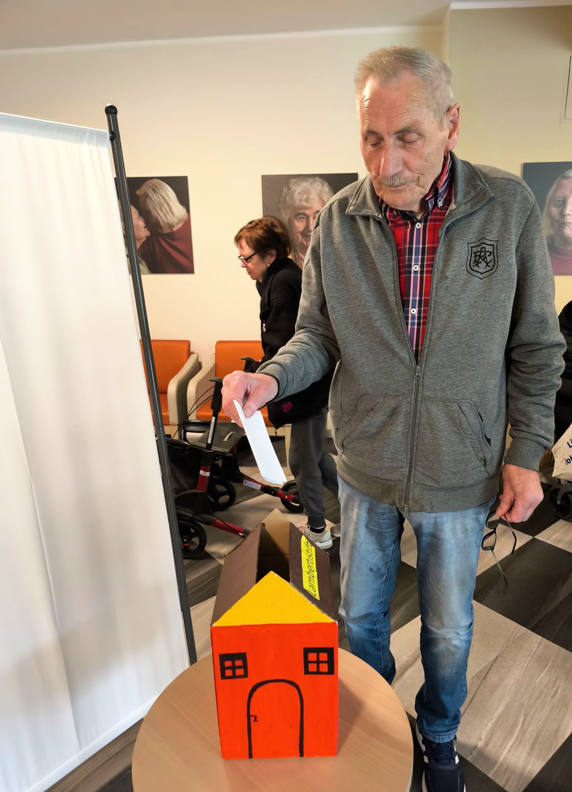Vorbereiteter Wahlbereich für die Heimbeiratswahl mit Wahlkabine, Wahlurne und Kandidatenübersicht.