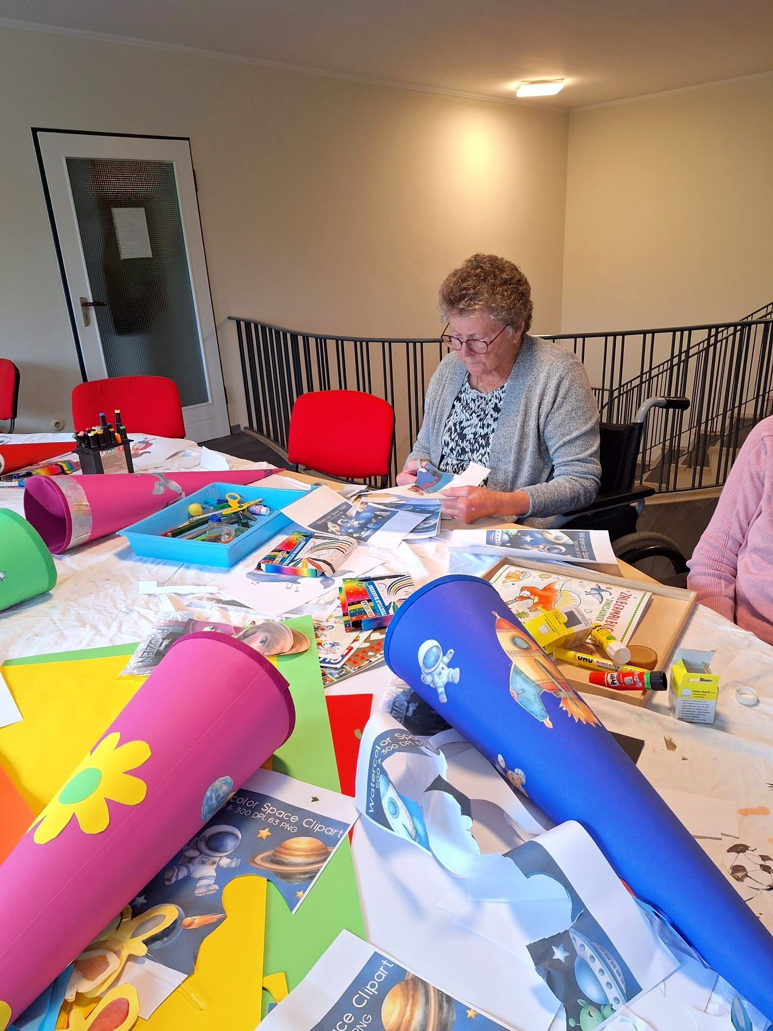 Bewohnerin bastelt bei der Aktion Schultüte gemeinsam mit Bastelmaterialien und bunten Schultüten am Tisch.