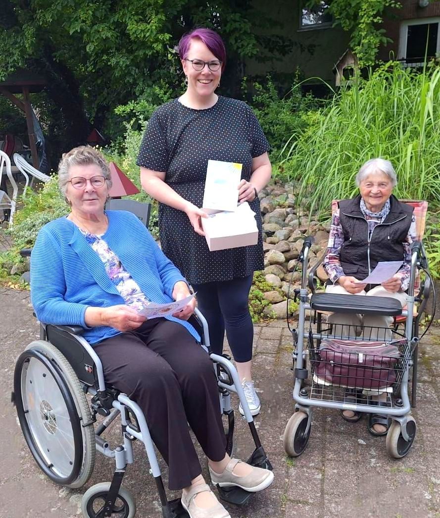Gruppenfoto im Garten des Lambertistifts mit Bewohnerinnen und Mitarbeiterin mit Karten aus der Aktion „Herzenspost“.