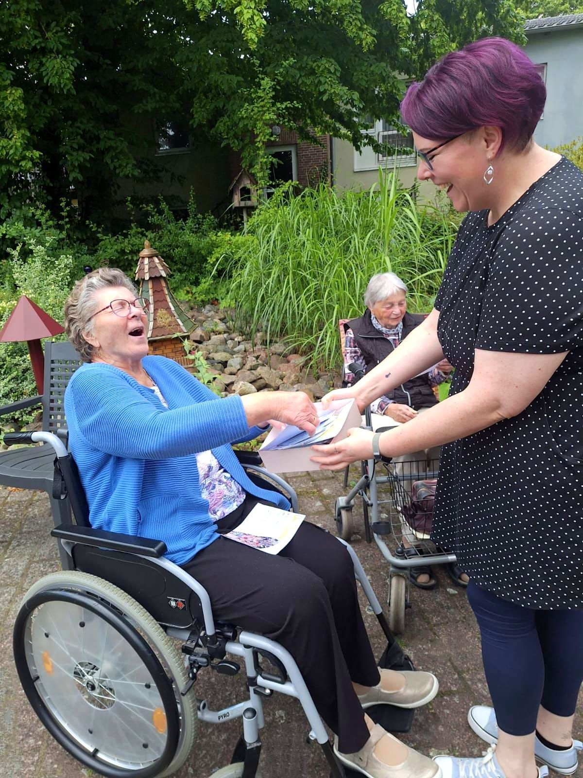 Mitarbeiterin der Caritas überreicht einer Bewohnerin im Garten des Lambertistifts Karten aus der Aktion „Herzenspost“.
