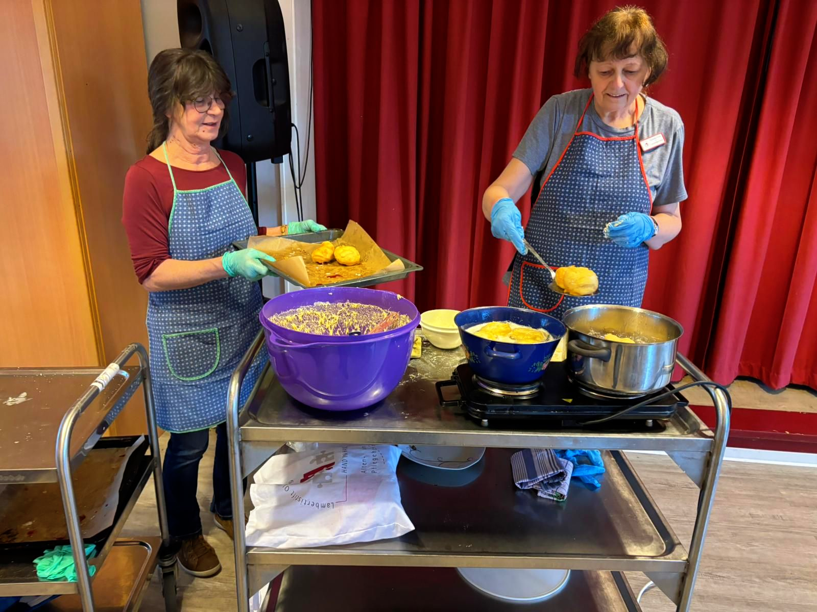 Frau Willms und Frau Peters backen gemeinsam Berliner an einem mobilen Kochwagen.