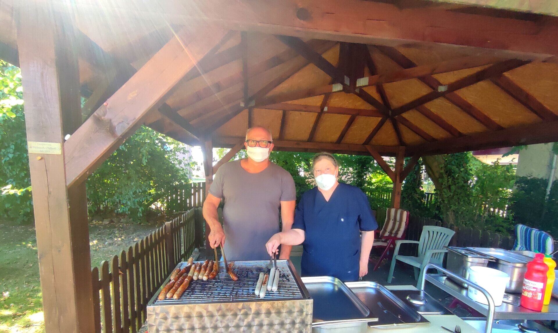 Zwei MitarbeiterInnen stehen an unserem Grill und grillen Bratwürstchen bei unserem Sommerfest.
