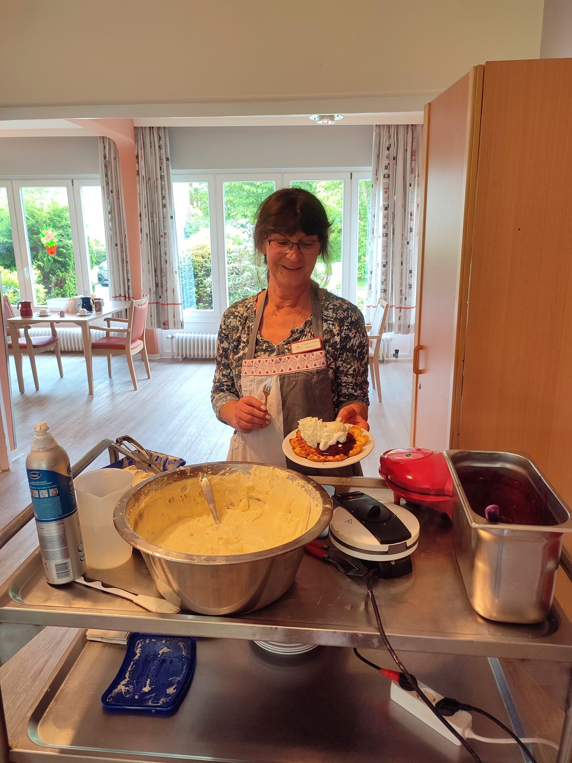 Frau Wilms vom Betreuungsteam serviert Waffeln mit Kirschen und Sahne.