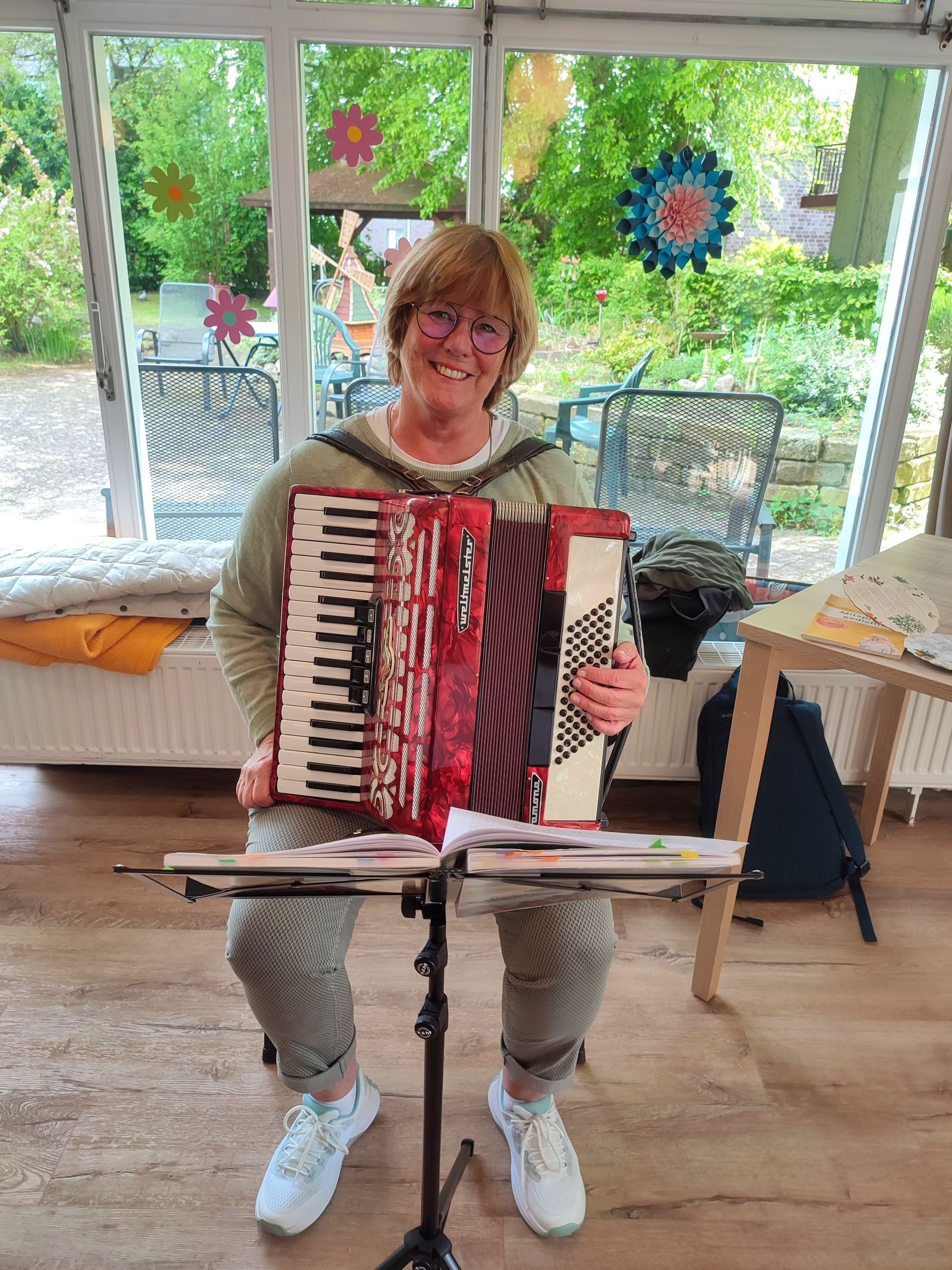 Ehrenamtliche Frau Munzel spielt Akkordeon im Tagesraum.