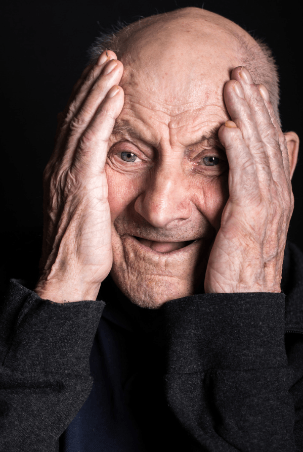 Älterer Mann hält sich lächelnd die Hände an den Kopf während eines Porträt-Fotoshootings von Soul-Photo.