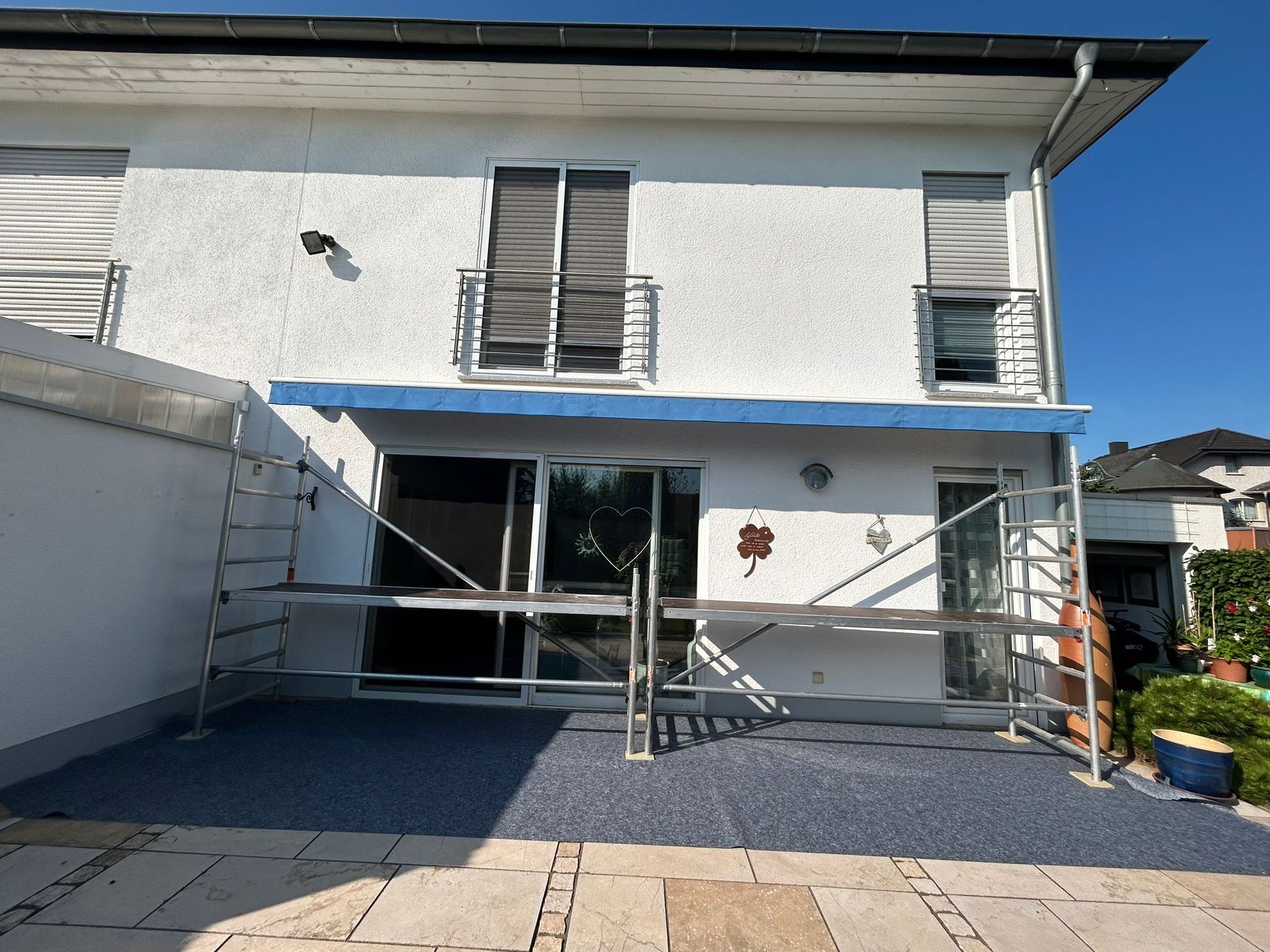 alte Markise alte offene Markise mit blauem Markisentuch an weißer Fassade, der Boden ist bereites ausgelegt und unser Gerüst aufgebaut.