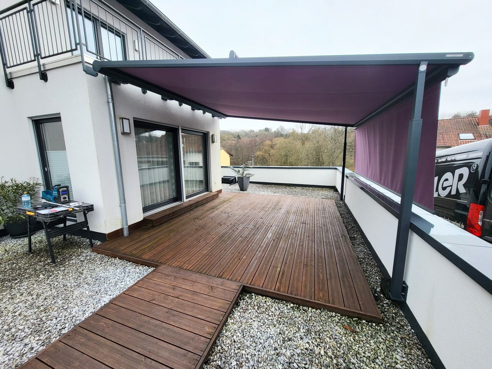 weinor_Markise_LED_neu_Saarland_Rolladen_Kessler Pergola-Markise am Erker montiert, überspannt mit ihrem lilafarbenen Tuch die komplette Holzterrasse.
