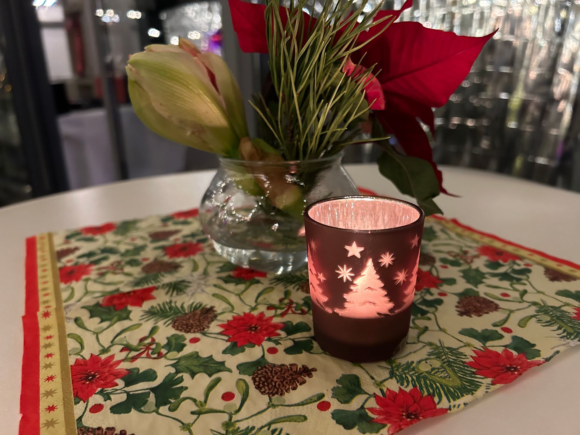 Alle Tische sind weihnachtlich dekoriert. Auf einem Stehtisch liegen Weihnachtsservietten, weihnachtliche Blumen und Teelichter stehen darauf. 