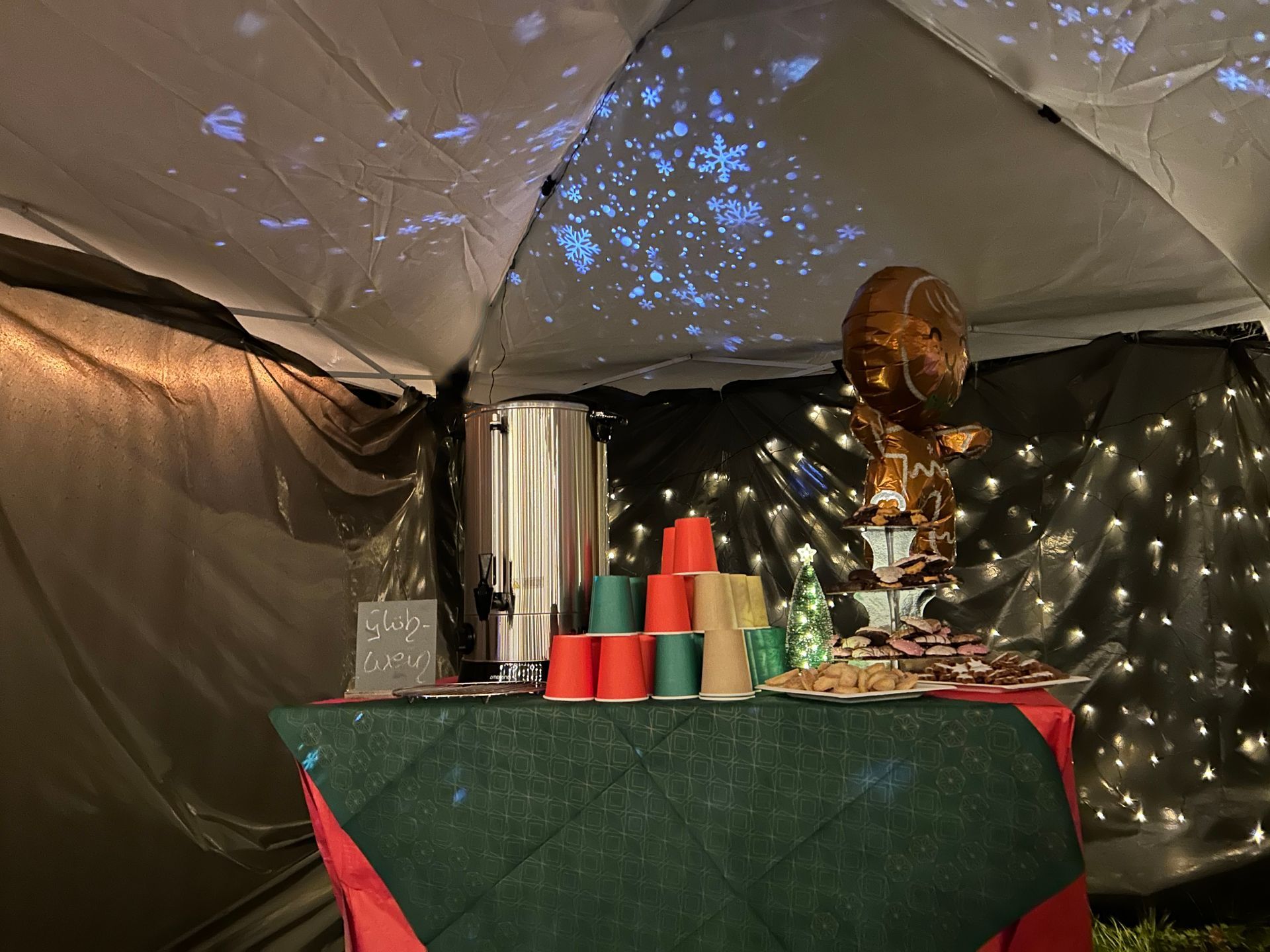Ein großer Wärmebehälter mit Glühwein steht auf dem Tisch im Zelt. Ein Projektor wirft weiße Sterne an den Himmel des Zeltes.