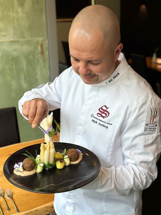 Küchenchef Maik Delling richtet ein Gericht sorgfältig auf schwarzem Teller an – Schlosscafé Teningen