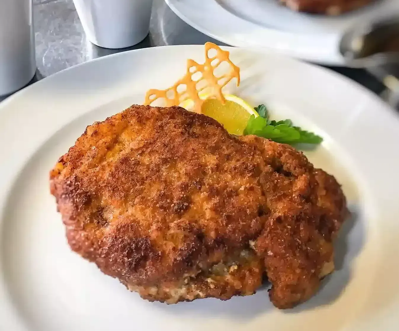 Knusprig gebratenes Schnitzel mit goldbrauner Panade auf weißem Teller – Schlosscafé Heimbach